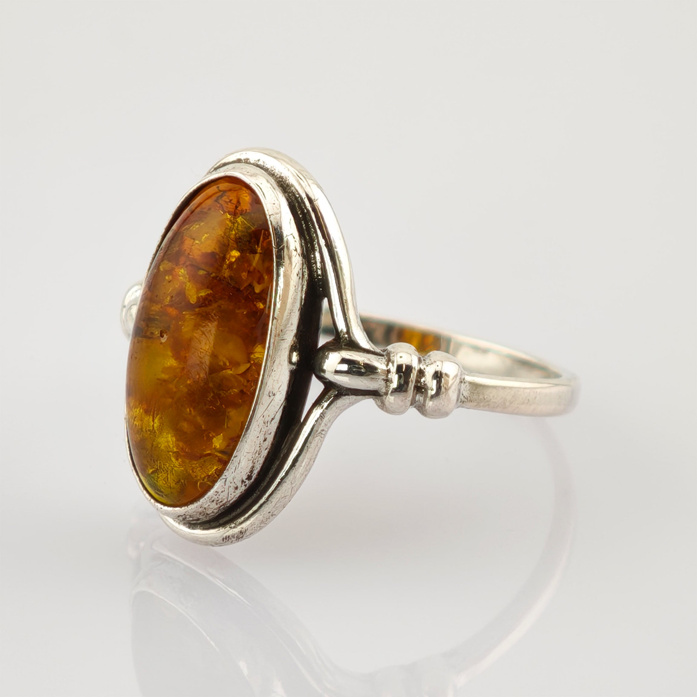 Silberring mit ovalem Bernsteinschmuck auf reflektierender Oberfläche.