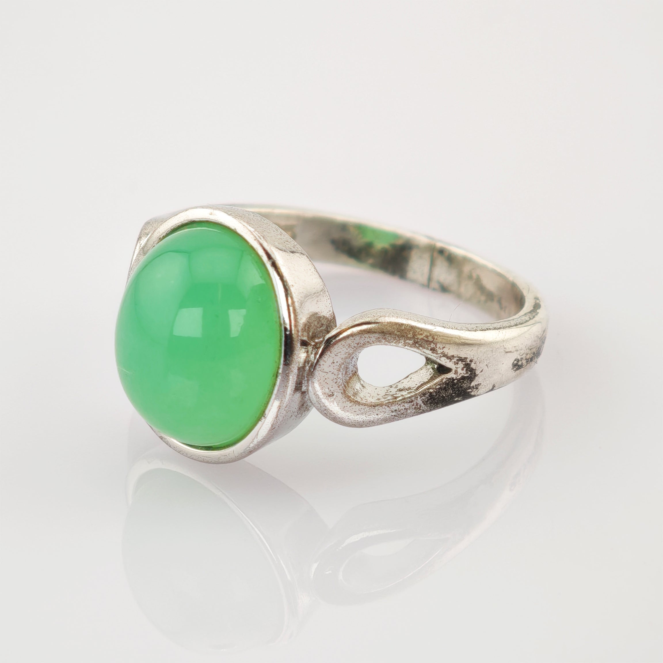 Silberring mit ovalem grünem Edelstein und tropfenförmigem Ausschnitt auf weißem Hintergrund