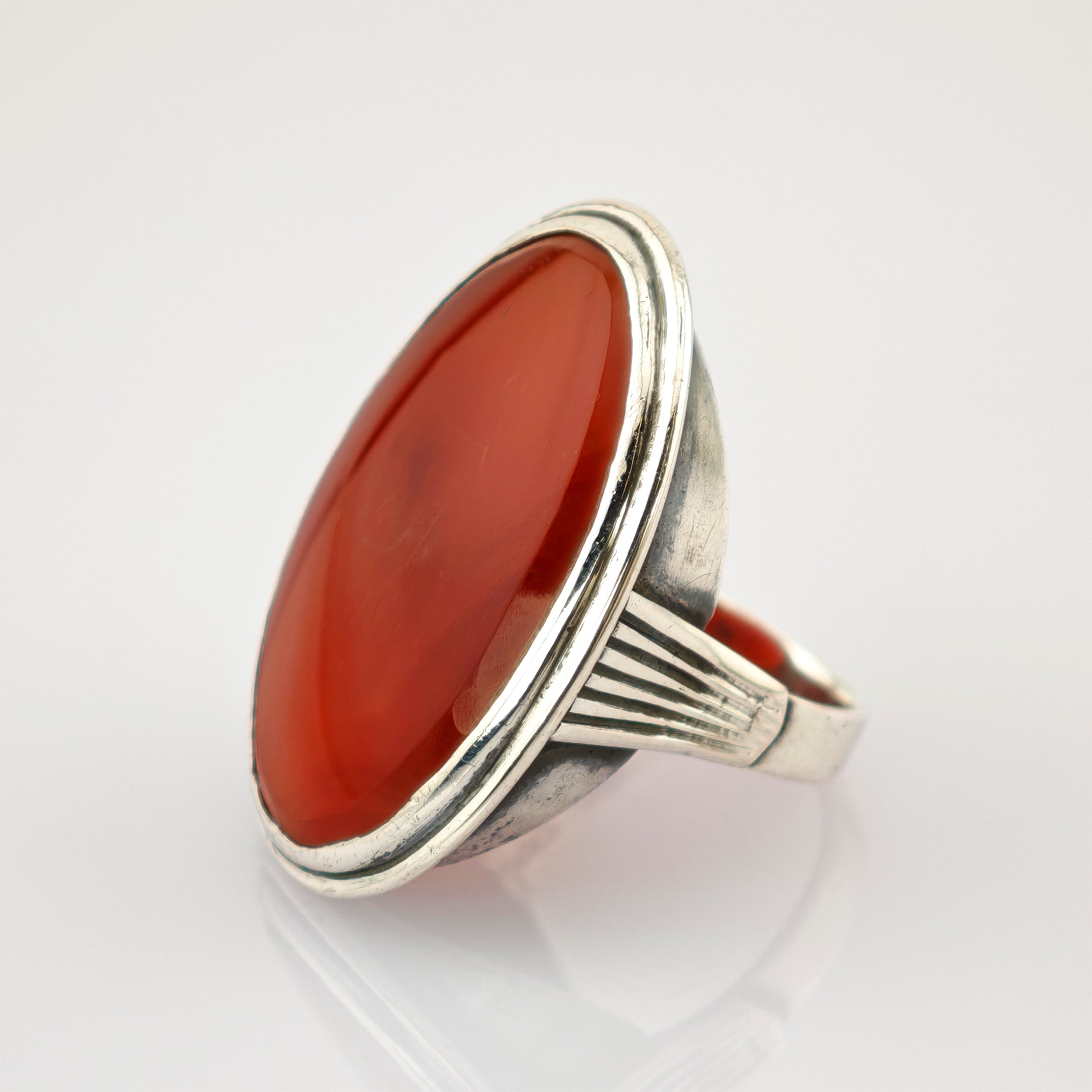 Silberring mit großem ovalem polierten Karneolstein und geriffeltem Band auf weißem Hintergrund