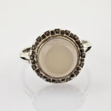 Fein gearbeiteter Silberring mit ovalem Mondstein in strukturiertem Rahmen auf weißem Untergrund.