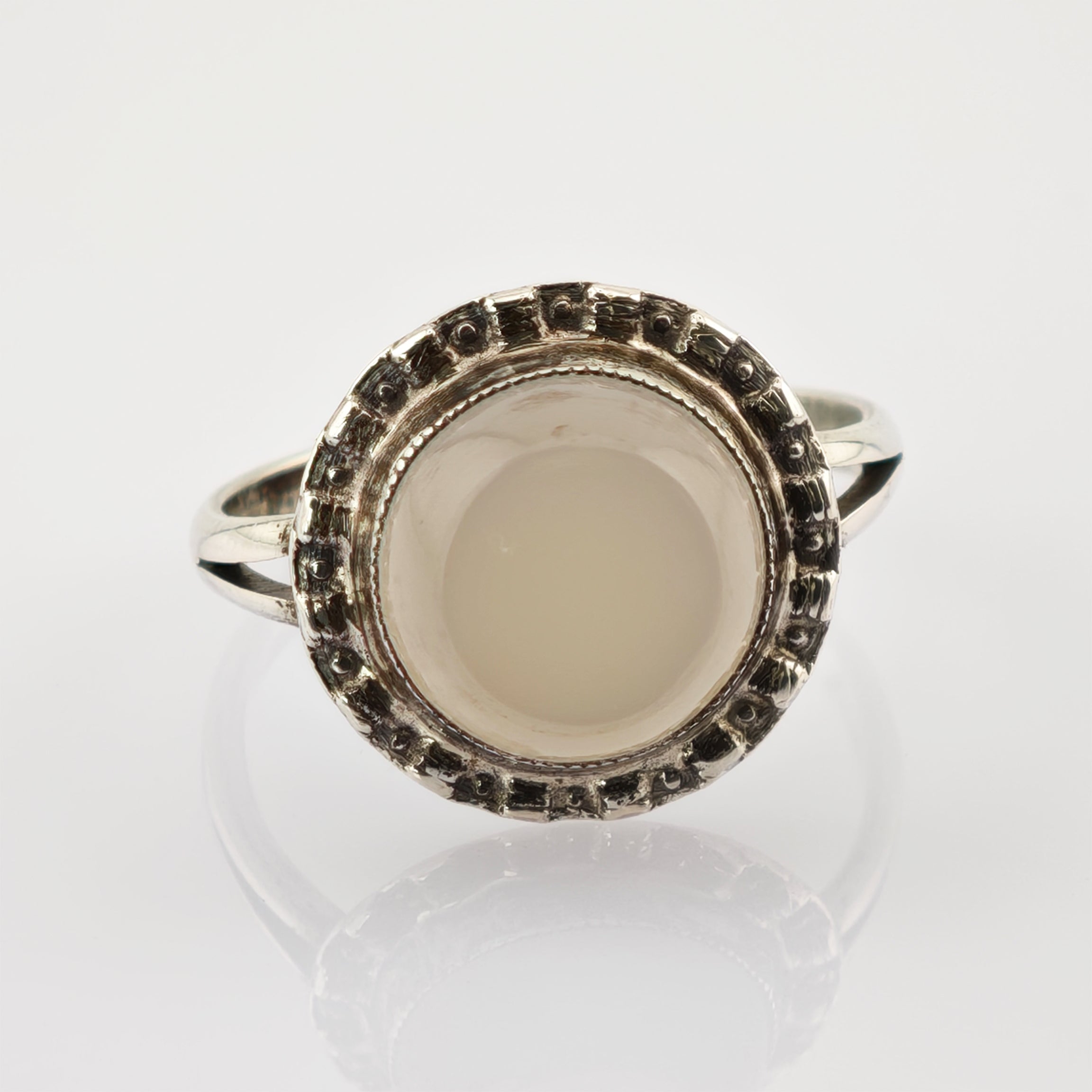 Fein gearbeiteter Silberring mit ovalem Mondstein in strukturiertem Rahmen auf weißem Untergrund.