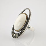 Silberring mit ovalem weißen Stein, umgeben von kleinen schwarzen Perlen.