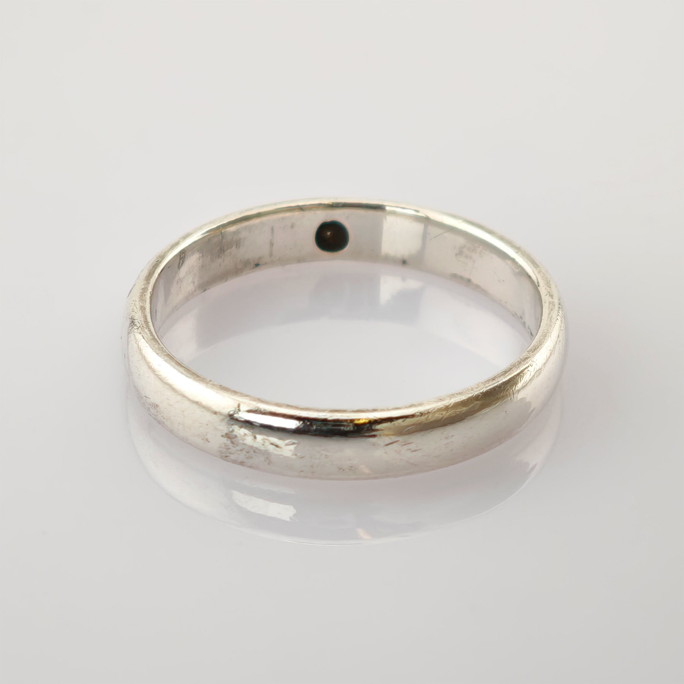 Schlichter Silberring mit polierter Oberfläche auf einer glänzenden weißen Fläche.
