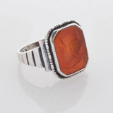Silberring mit rechteckigem rot-orangefarbenem Edelstein und geripptem Band, graviert mit Flügelhelm und 925 Stempel.