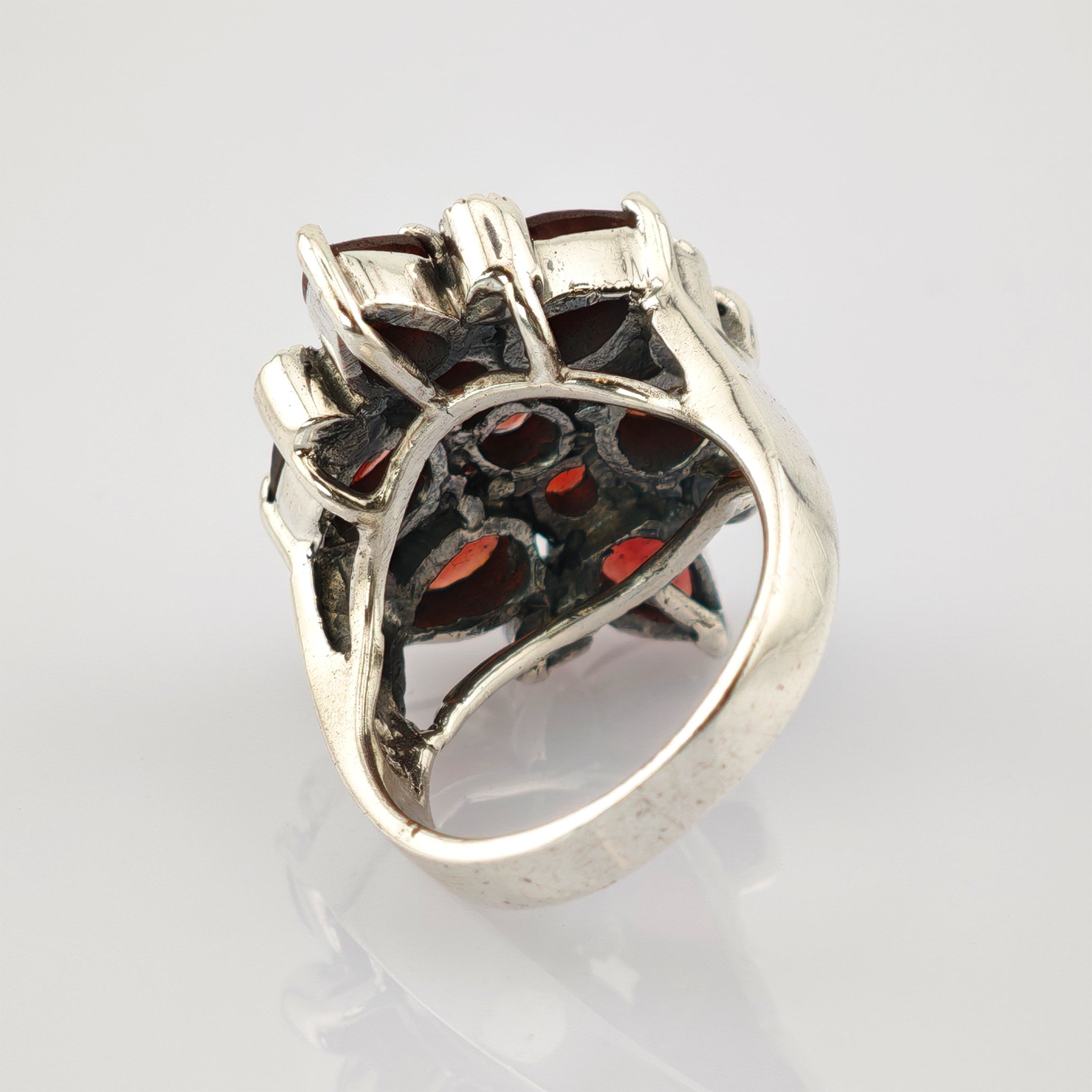 Silberring mit detailliertem Seitenmuster und rubinroten Steinen auf reflektierender weißer Oberfläche