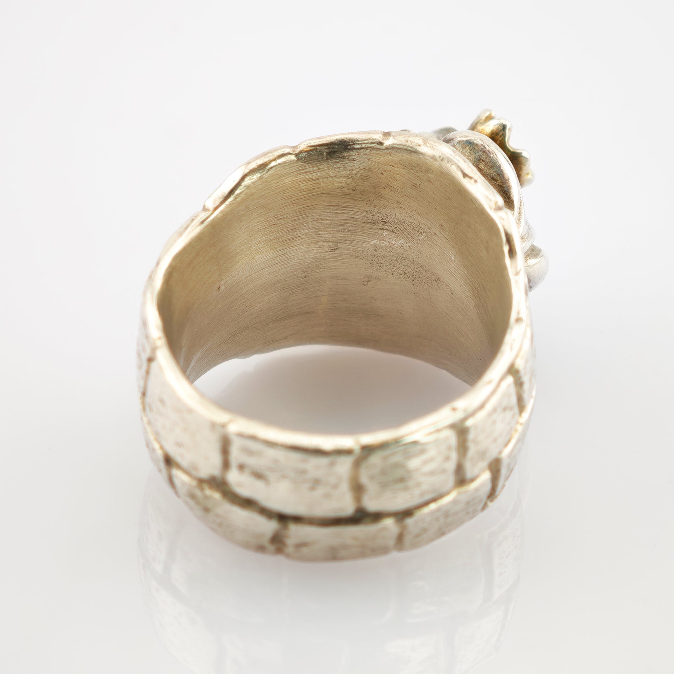 Silberring mit strukturierter Oberfläche im Steinmuster vor reflektierendem weißen Hintergrund.