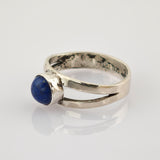 Silberring mit tiefblauem, rundem Stein und geteilter Ringschiene auf weißem Hintergrund.