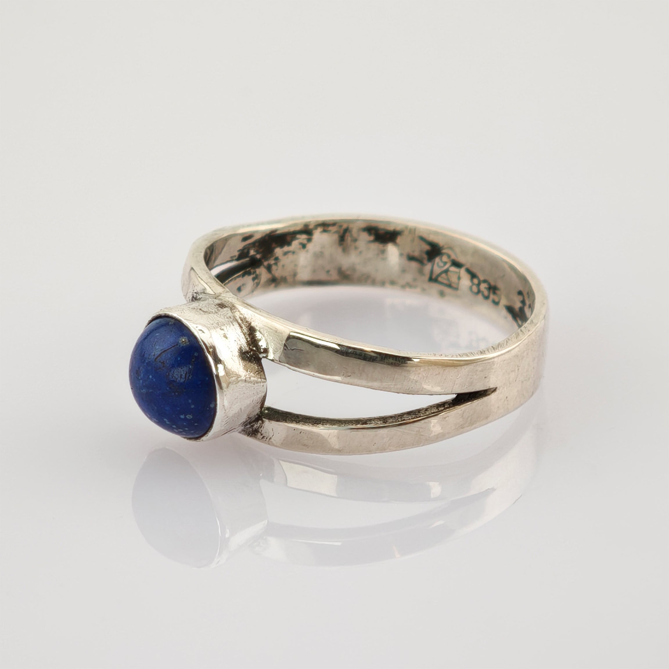 Silberring mit tiefblauem, rundem Stein und geteilter Ringschiene auf weißem Hintergrund.