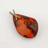 Teardropförmiger Bernsteinanhänger mit silberner Öse und dunklen Einschlüssen im warmen orangefarbenen Bernstein.