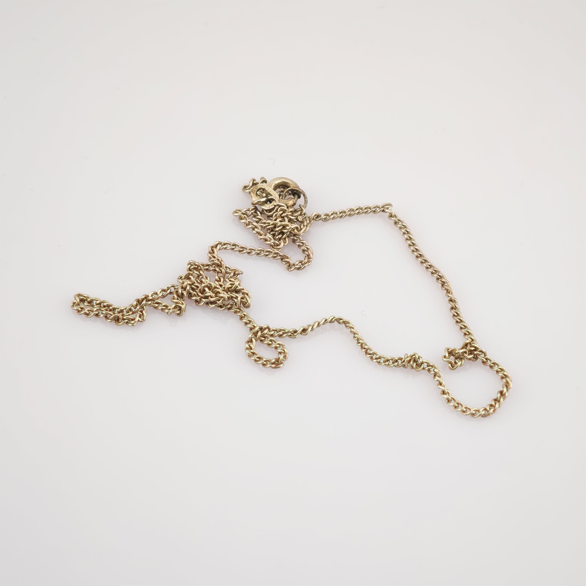 Verheddertes Goldkettchen mit verdrehten Gliedern und rundem Verschluss auf weißem Hintergrund