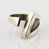 Verstellbarer Metallring mit glattem Außenband und strukturiertem dreieckigem Einsatz mit Patina.