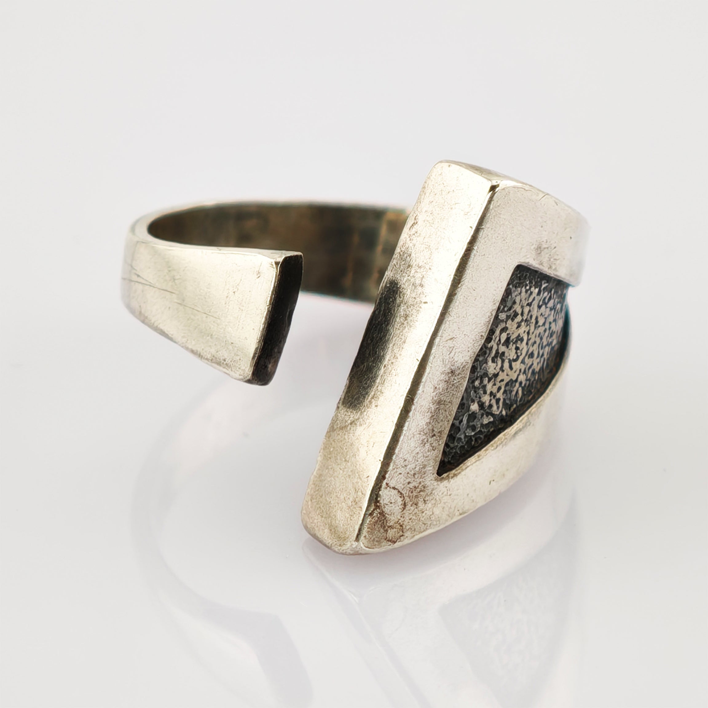 Verstellbarer Metallring mit glattem Außenband und strukturiertem dreieckigem Einsatz mit Patina.