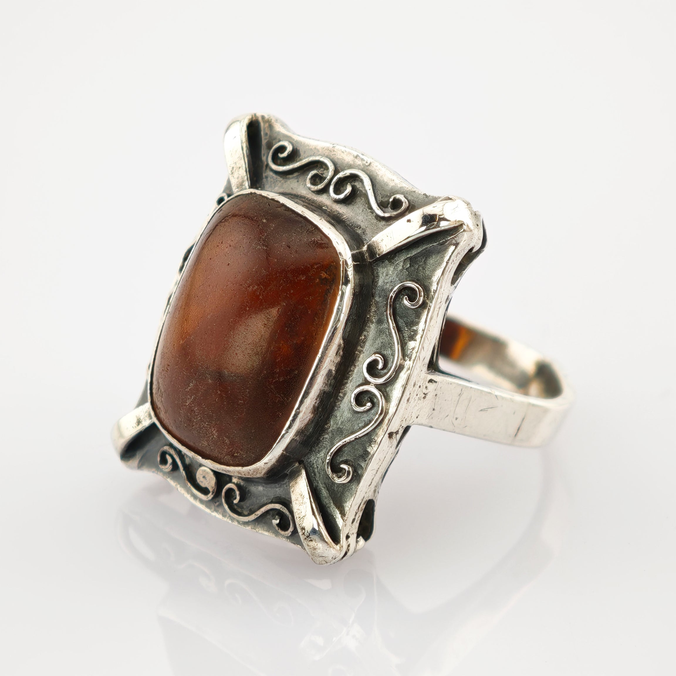 Rechteckiger Vintage-Ring mit poliertem braunem Bernstein und silbernem Rahmen mit Wirbelmustern.