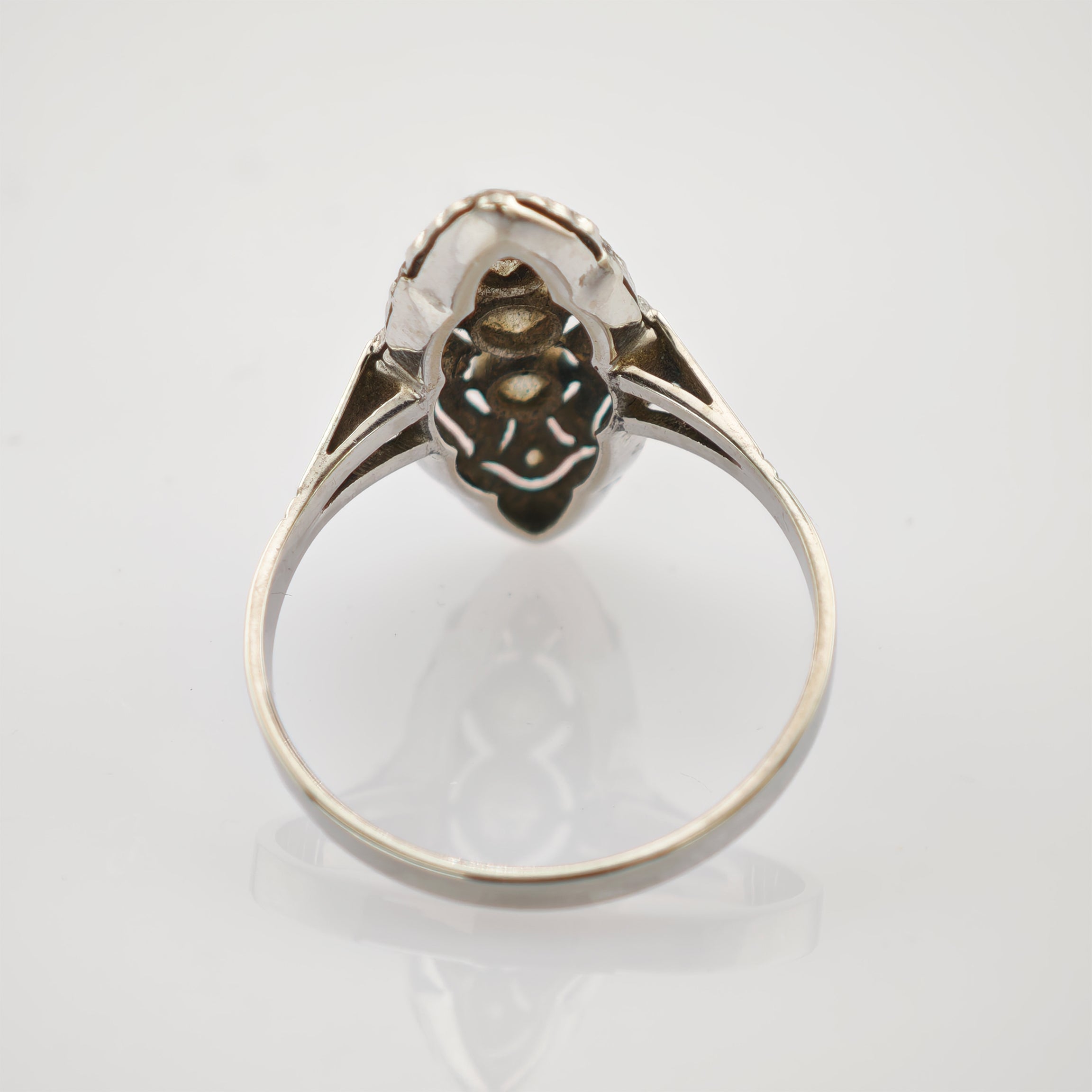 Vintage-Silberring mit kunstvollem Ringkopf und Schulterdetail auf reflektierender Oberfläche.