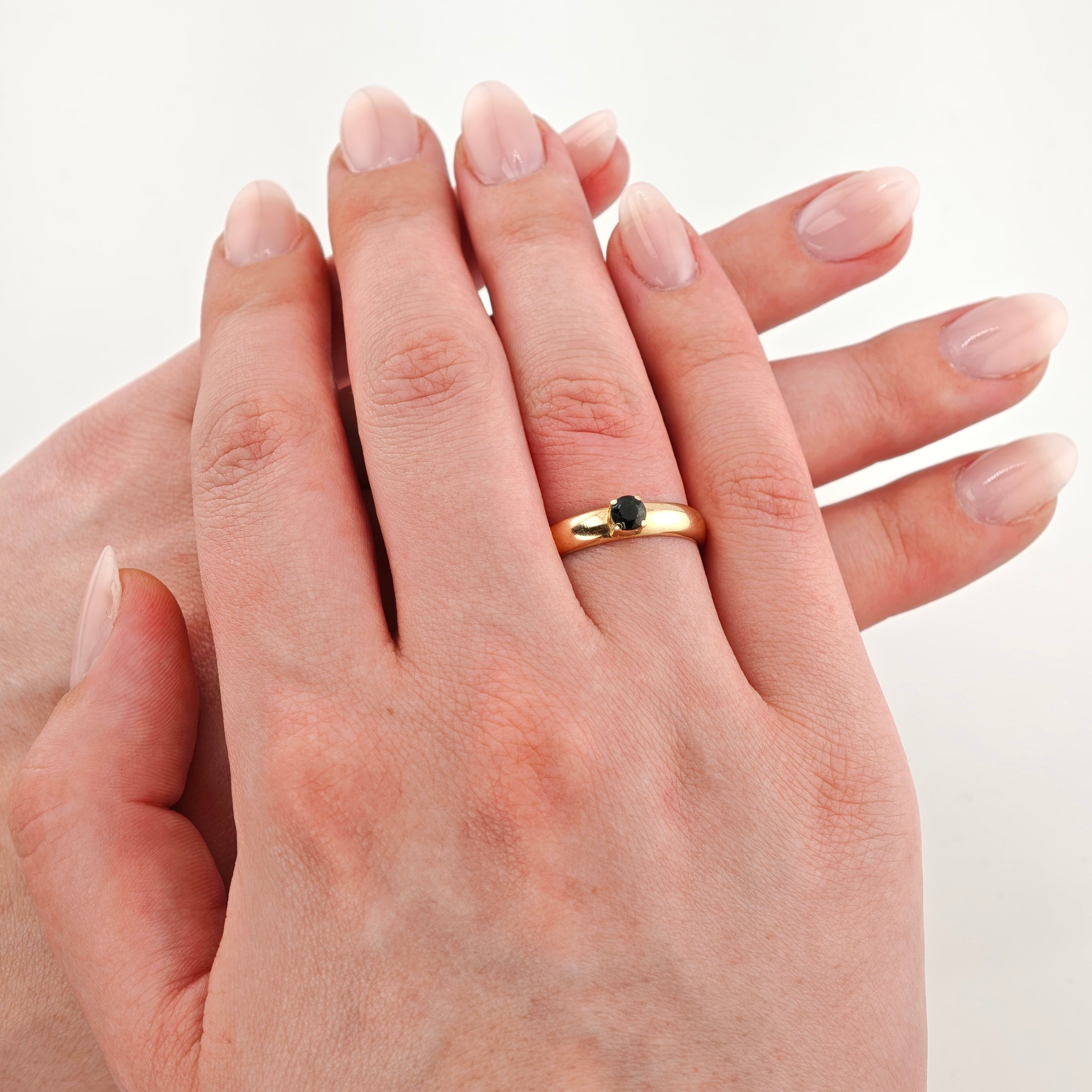 Zwei Hände aufeinandergelegt, eine mit Goldring und schwarzem Stein am Ringfinger, vor weißem Hintergrund.