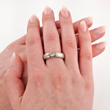 Nahaufnahme von zwei Händen, obere Hand mit glänzend lackierten rosa Nägeln und silbernem Ring mit klarem Edelstein.