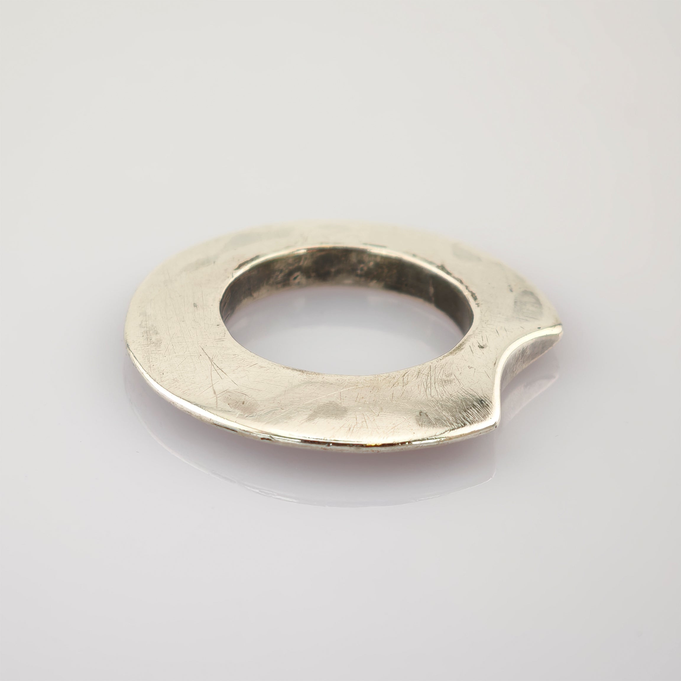 Abgenutztes silbernes Objekt in Ringform mit kleiner Kerbe auf weißem Hintergrund