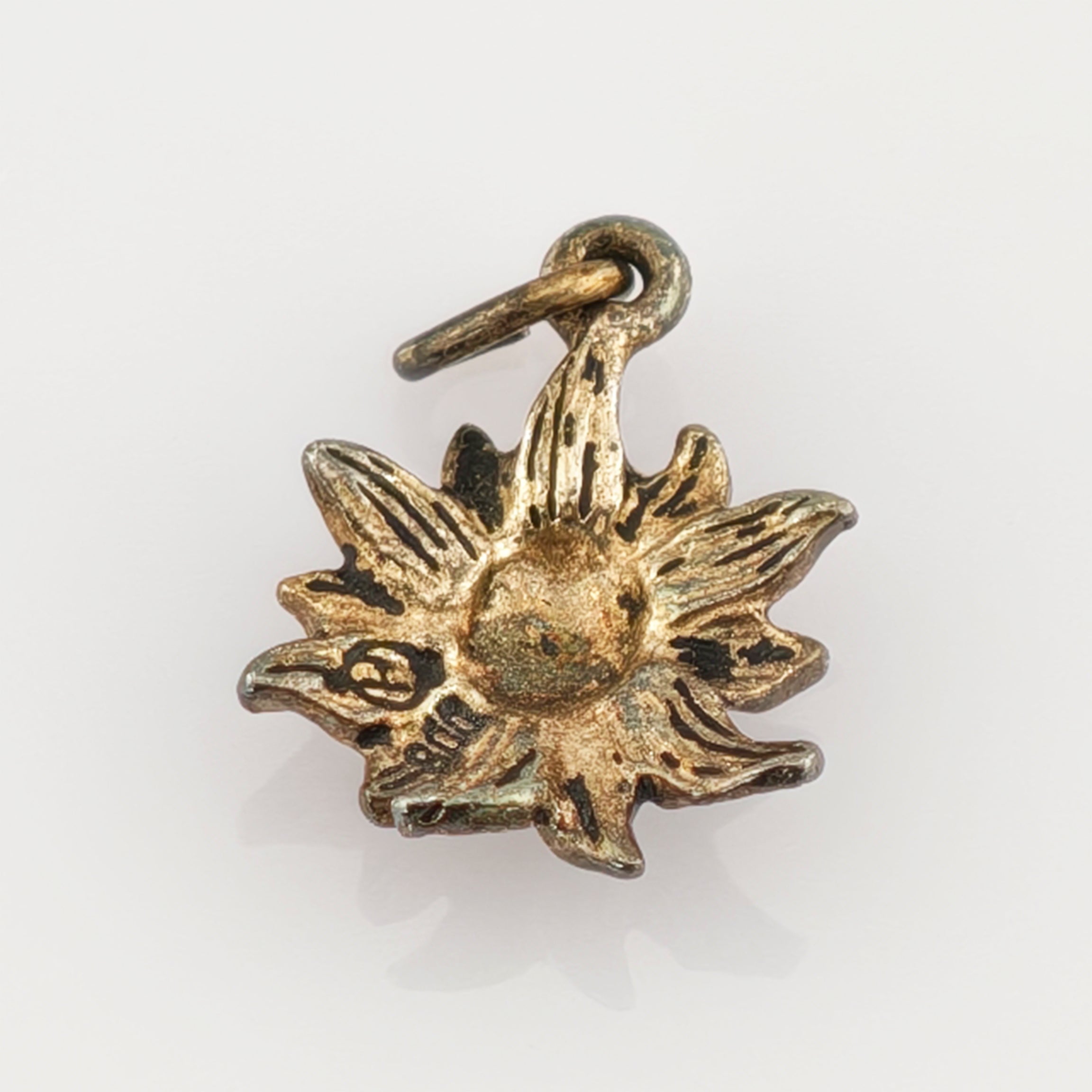 Kleiner Metallanhänger in Form einer stilisierten Blume mit acht texturierten Blättern und schwarz-goldener Patina.