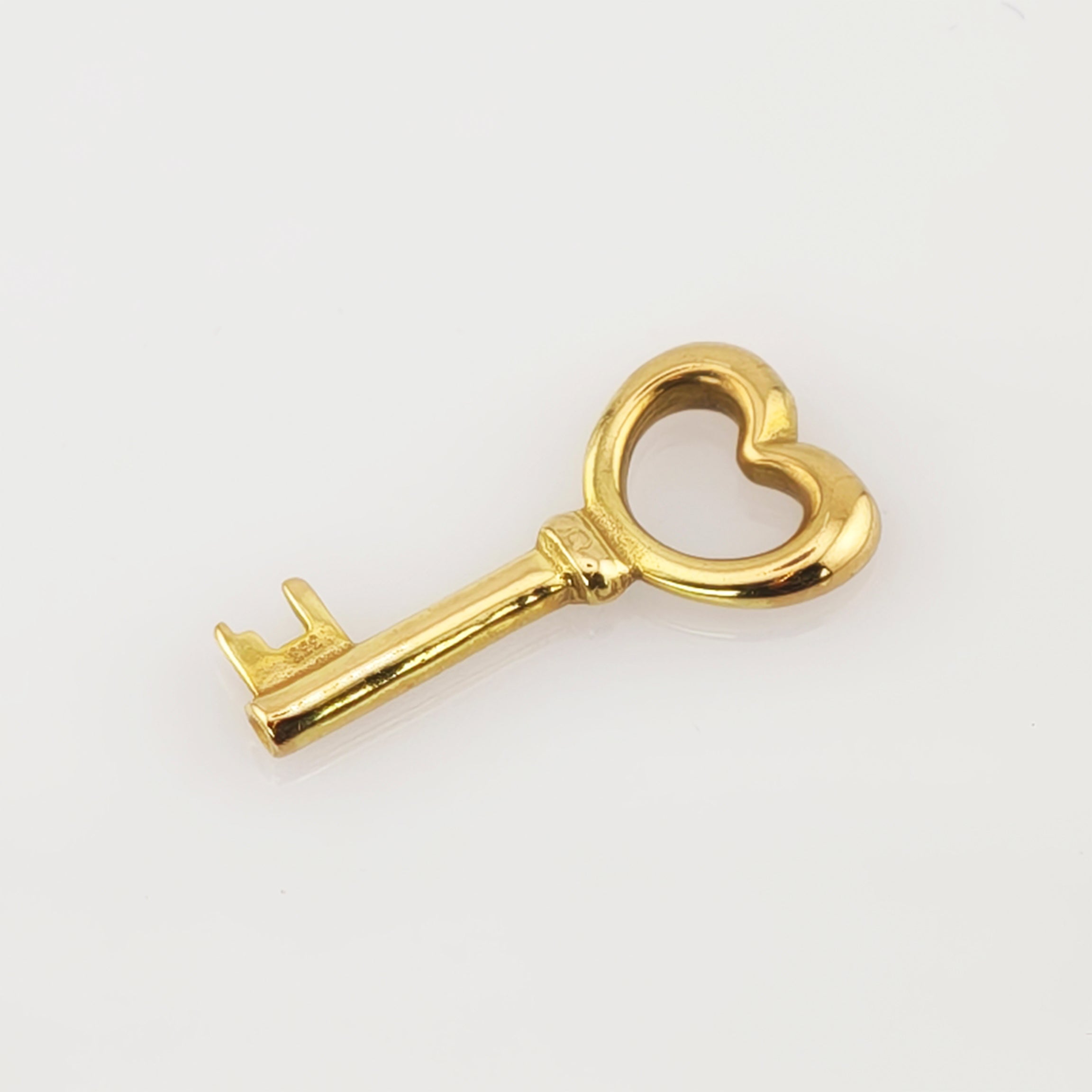 Kleiner goldener Schlüssel mit herzförmigem Griff auf weißem Hintergrund.