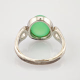 Antiker Silberring mit rundem grünem Edelstein auf einer reflektierenden weißen Oberfläche.