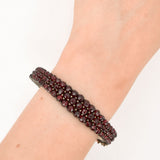 Antikes Armband mit drei Reihen tiefroter Granatsteine auf oxidiertem Metallsockel und kleiner Sicherheitskette, getragen am Handgelenk
