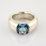 Breiter silberner Ring mit kissenförmigem, facettiertem blauen Edelstein und polierter Oberfläche