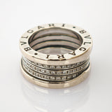 Detaillierte Nahaufnahme eines silberfarbenen Rings mit eingraviertem Bvlgari-Logo und 18K-Goldpunze auf reflektierender Oberfläche.