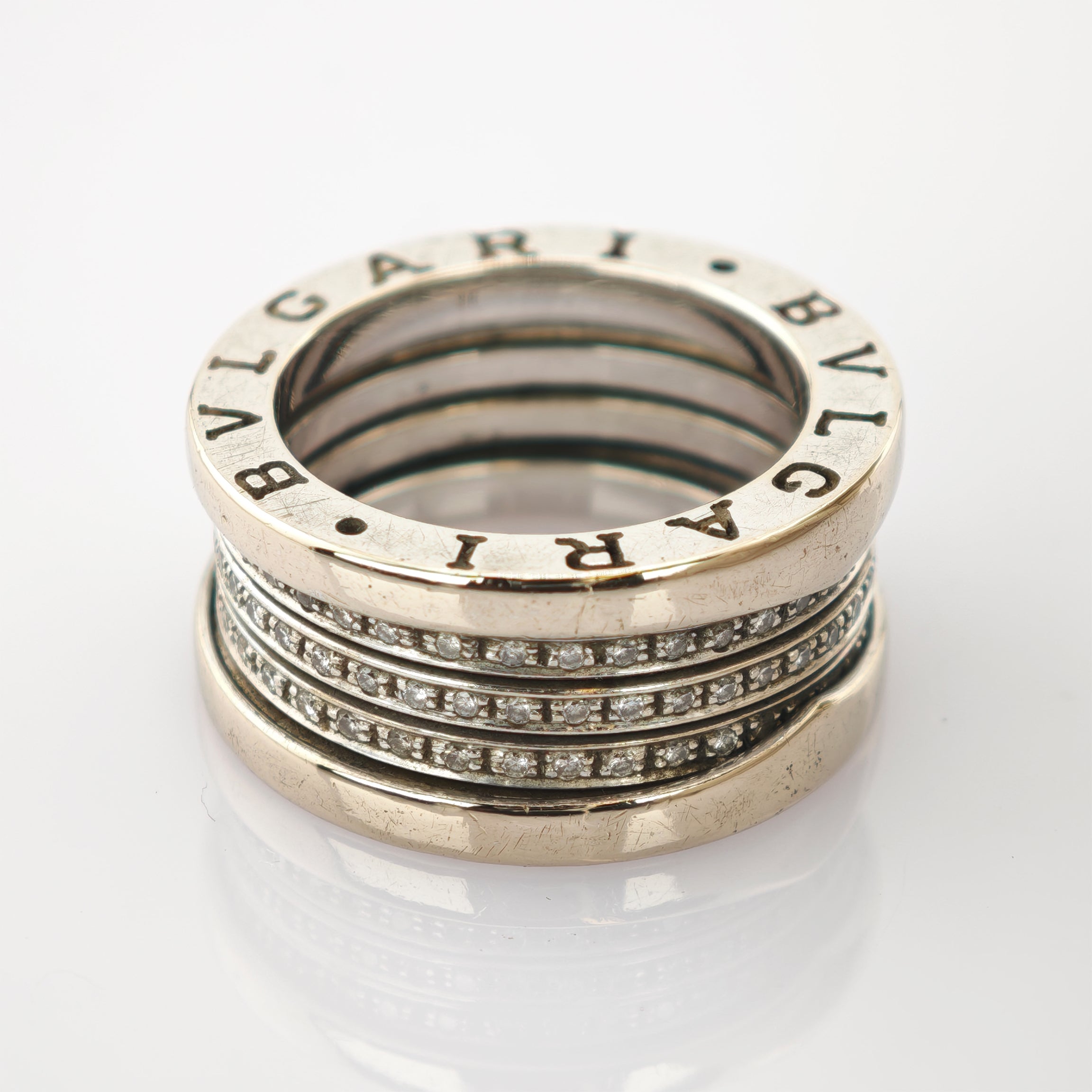 Detaillierte Nahaufnahme eines silberfarbenen Rings mit eingraviertem Bvlgari-Logo und 18K-Goldpunze auf reflektierender Oberfläche.