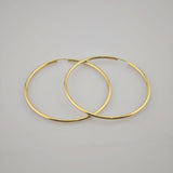 Zwei große, goldene Creolen auf weißem Untergrund, nebeneinander.