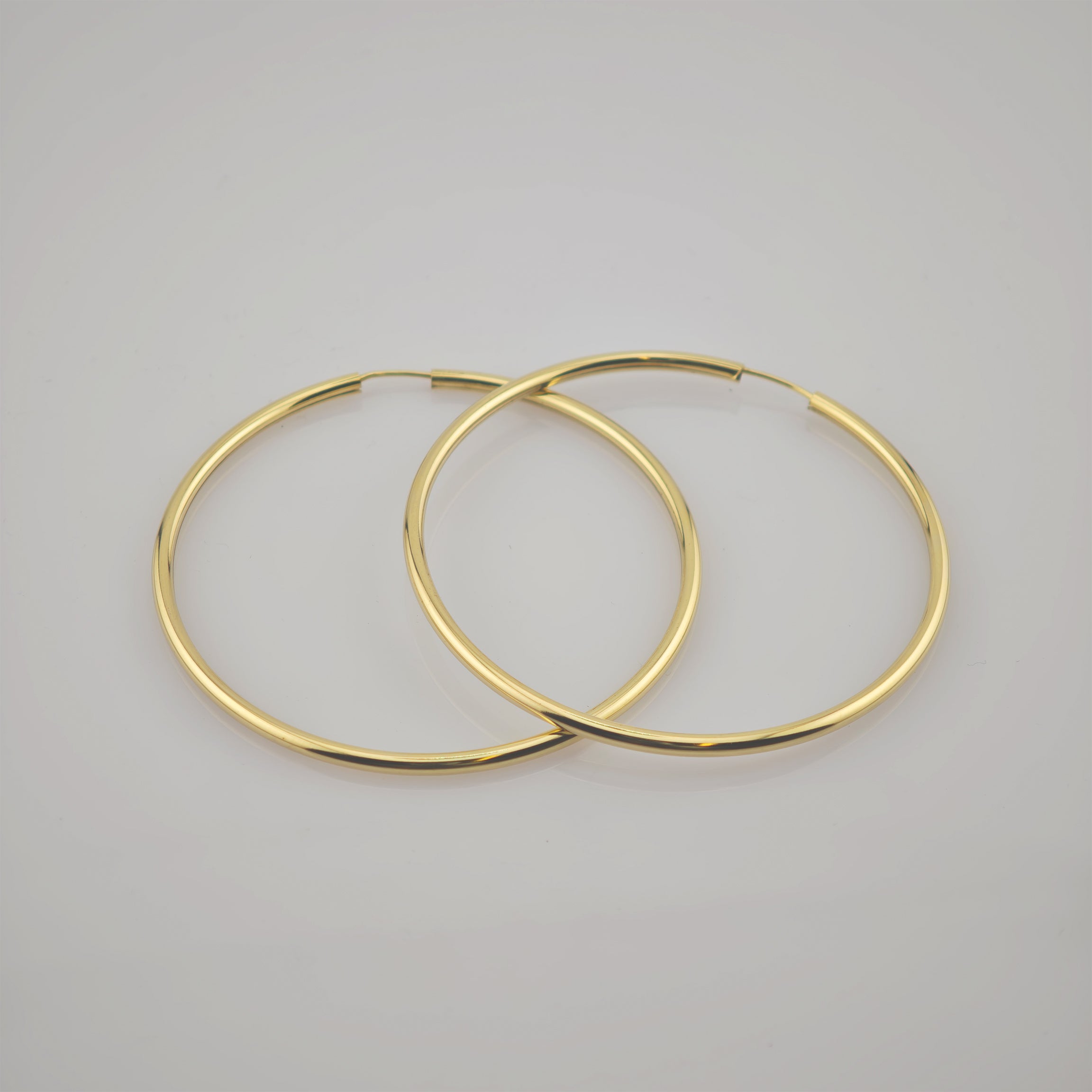 Zwei große, goldene Creolen auf weißem Untergrund, nebeneinander.