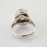 Detaillierter Silberring mit geteiltem Ringband auf reflektierender weißer Oberfläche.