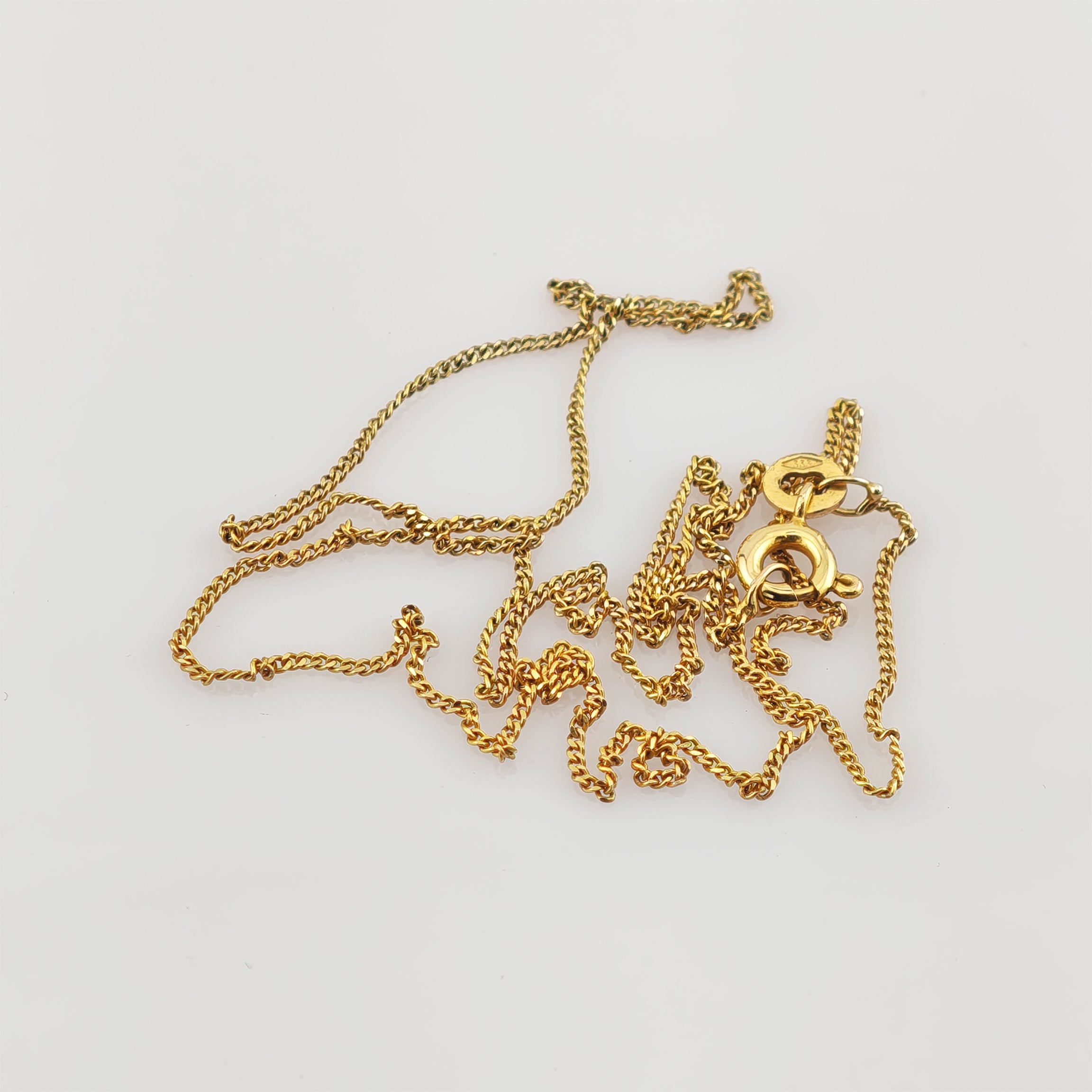 Dünne Goldkette mit rundem Verschluss auf weißem Hintergrund.