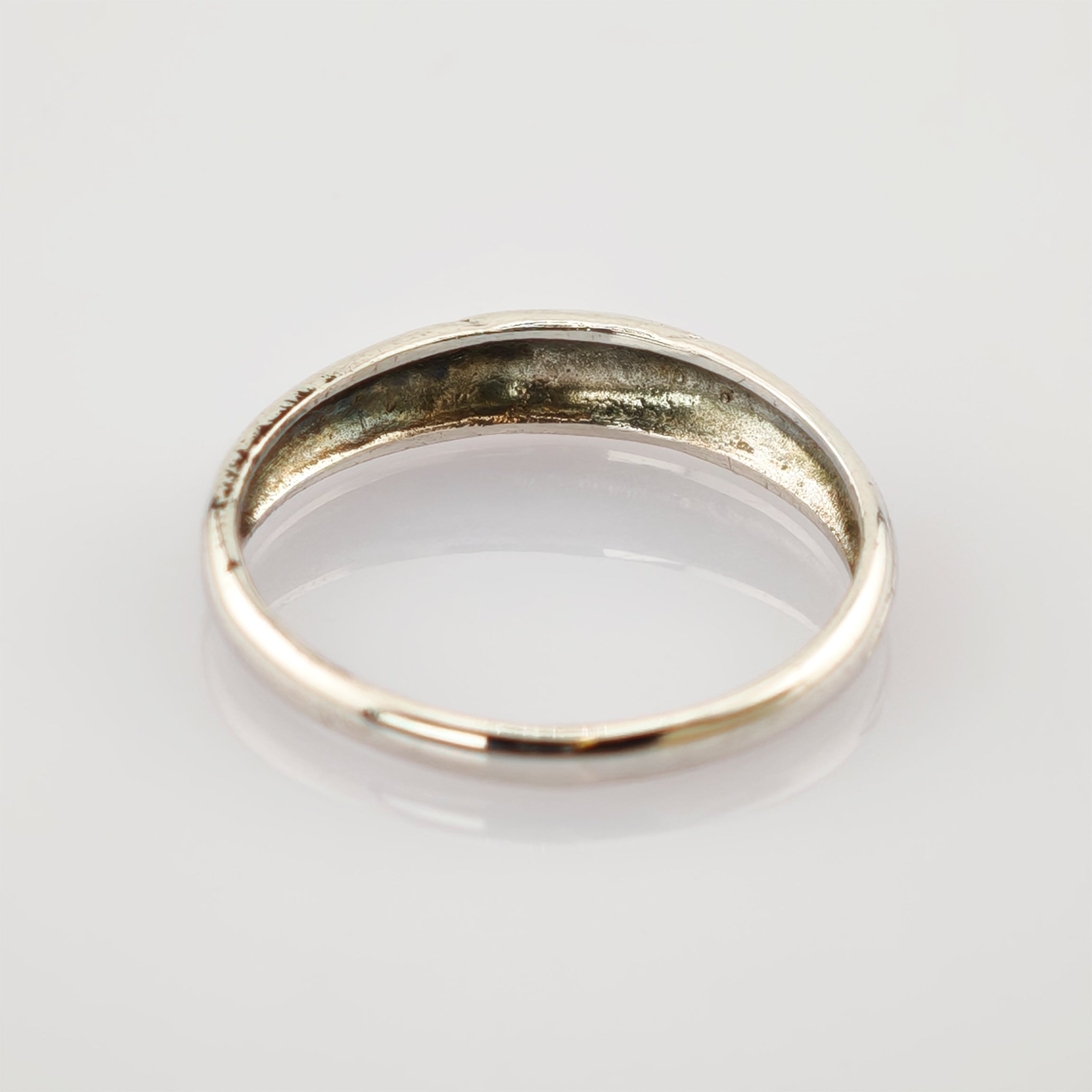 Einfacher silberner Ring mit leichten Anlaufspuren und kleinen Kratzern auf weißem reflektierendem Hintergrund.