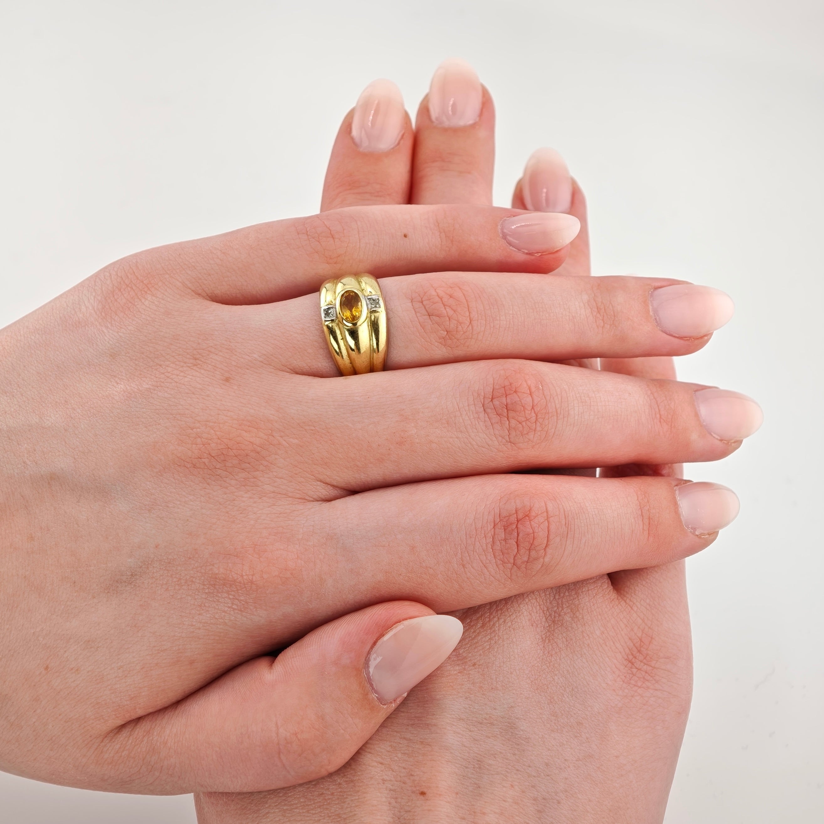 Zwei elegante Frauenhände mit nude rosa Maniküre und Goldring mit ovalem gelbem Edelstein und kleinen Diamanten.