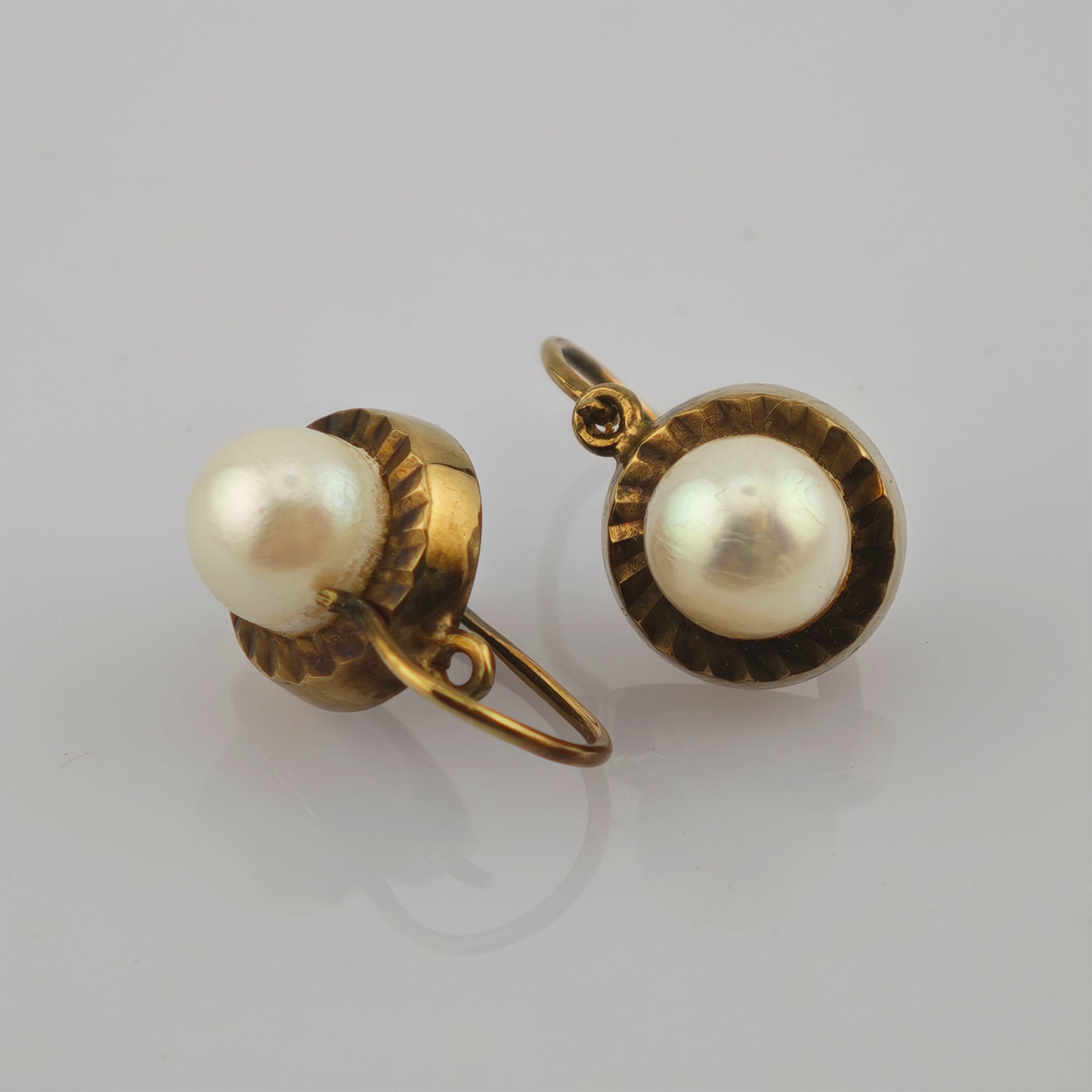 Paar elegante goldene Ohrringe mit großen runden weißen Perlen und geriffeltem Goldsockel