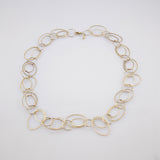 Elegante Halskette aus ovalen Goldringen mit strukturierter Oberfläche vor grauem Hintergrund.