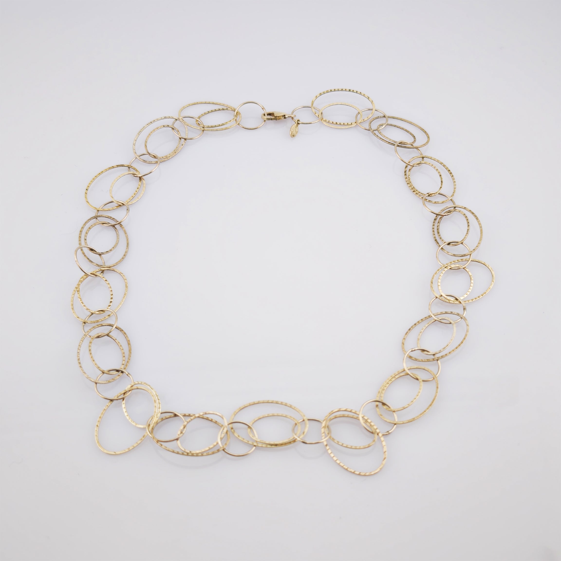 Elegante Halskette aus ovalen Goldringen mit strukturierter Oberfläche vor grauem Hintergrund.