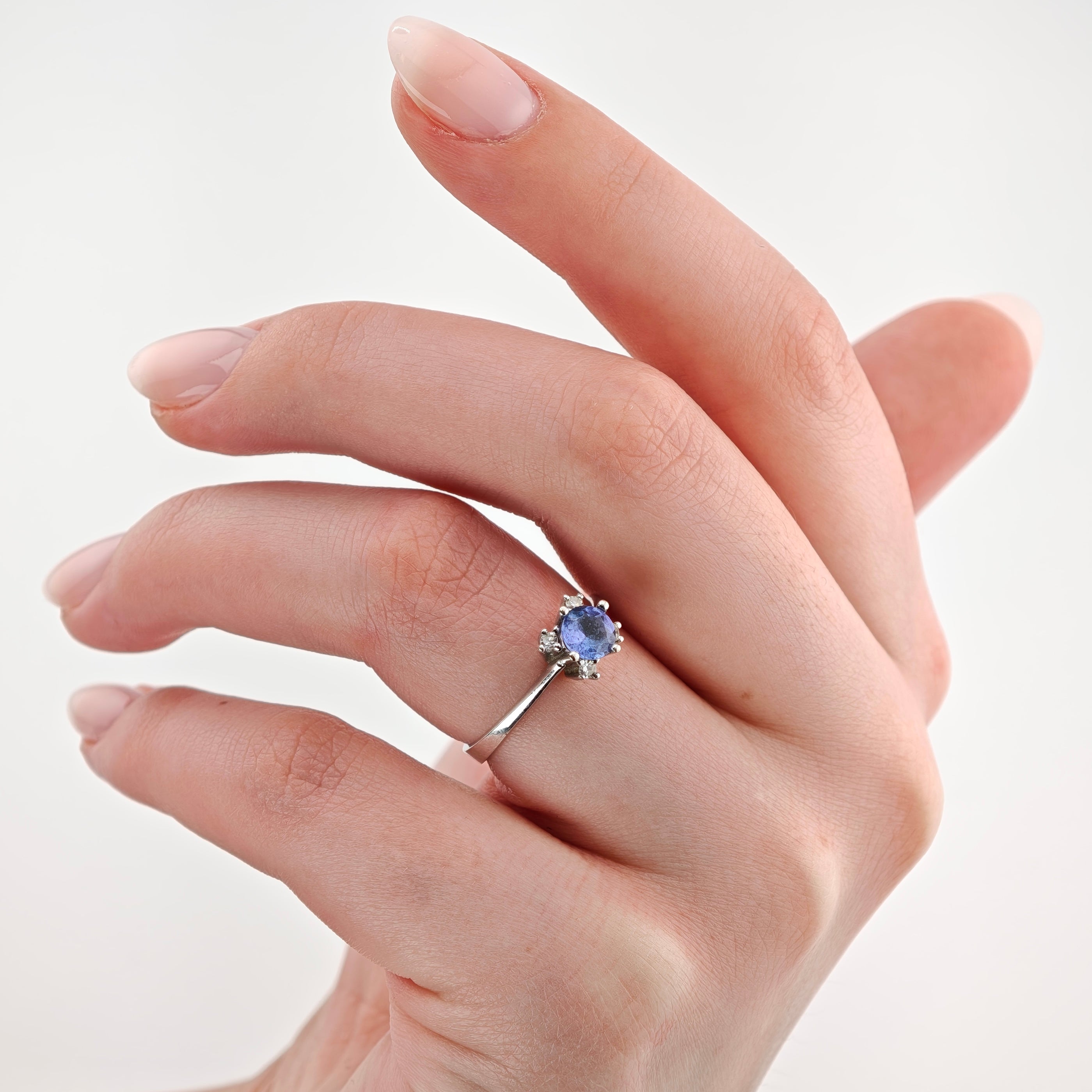 Elegante Hand mit Silberring und blauem Edelstein auf weißem Hintergrund.