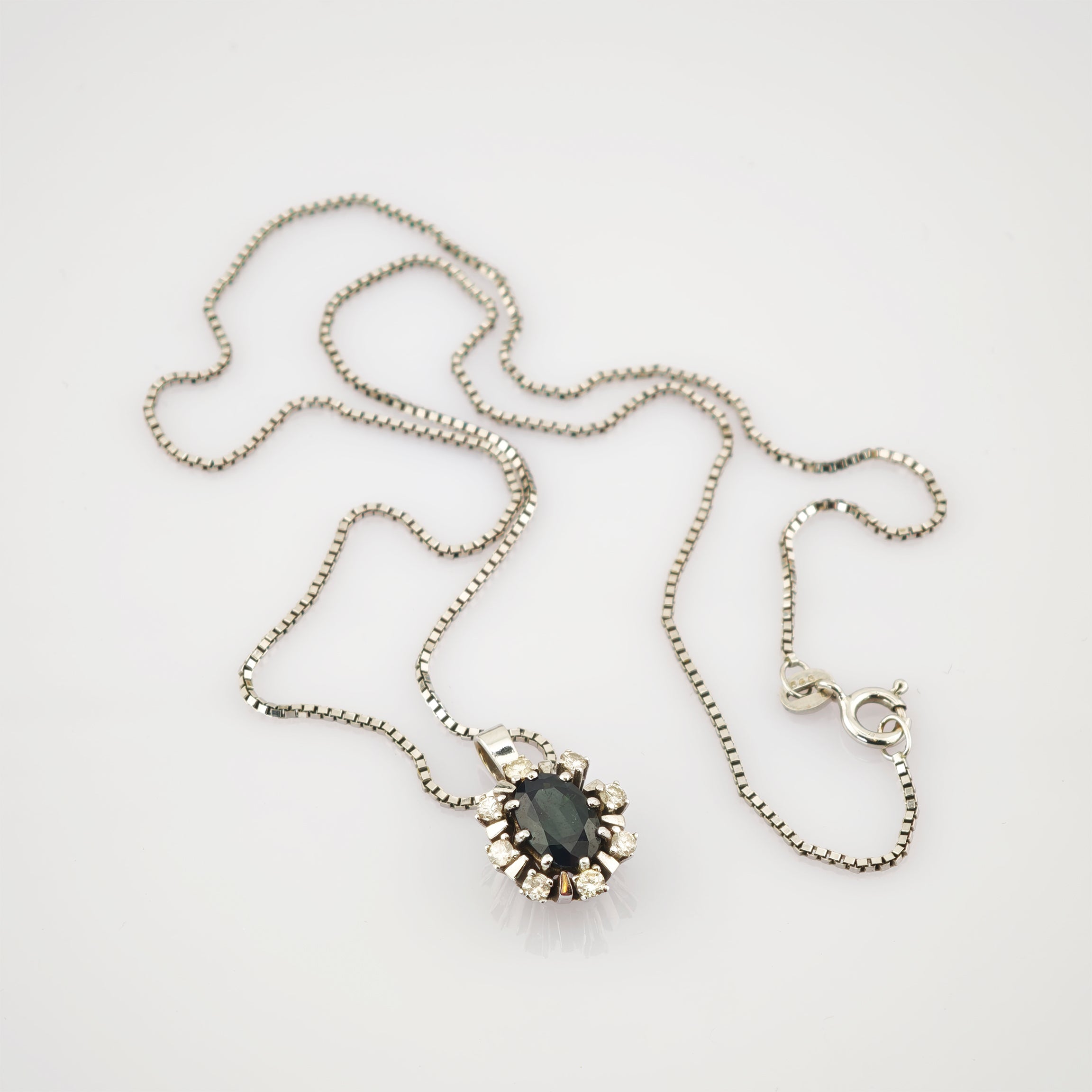 Elegante Silberkette mit blumenförmigem Anhänger aus dunklem ovalem Stein, umgeben von kleinen klaren Steinen.