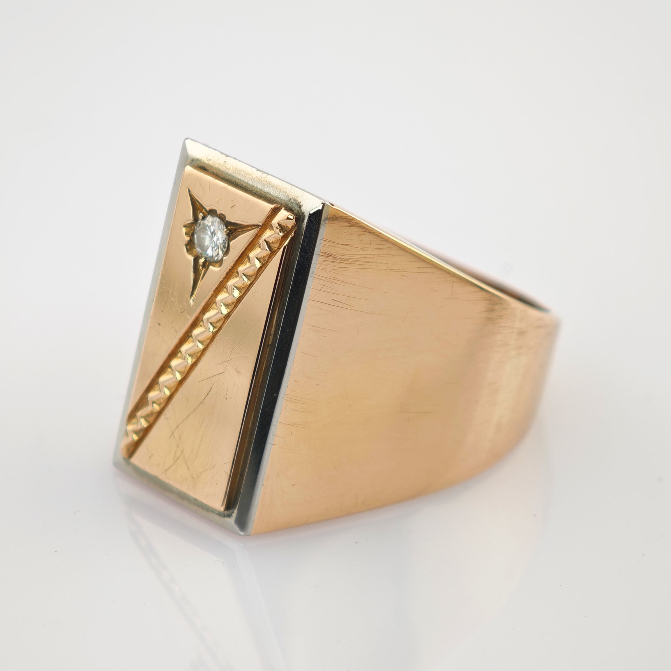 Goldener Ring mit rechteckigem Gesicht, kleinem Diamanten und diagonaler Textur auf glänzendem Eleganter Goldring mit rechteckiger Oberseite, Diamant in Sternformgravur und diagonal strukturierter Leiste.