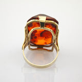 Eleganter Ring mit rechteckigem Bernstein und Goldfassung auf weiß reflektierender Oberfläche.