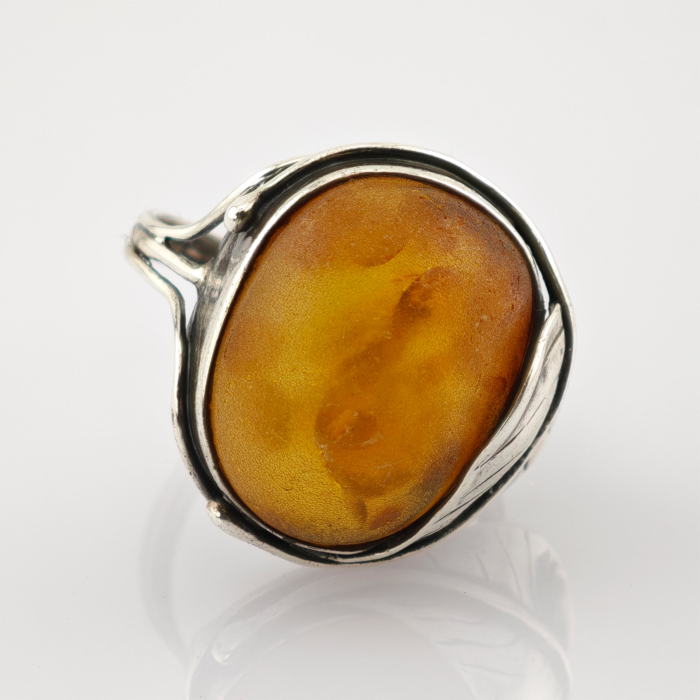 Eleganter Silberring mit großem ovalem Bernstein in honigbrauner Farbe und Blattmotiv im Rahmen.