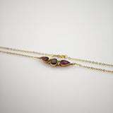 Elegantes Goldarmband mit drei dunkelroten Edelsteinen in Tropfen- und runder Form auf weißem Hintergrund