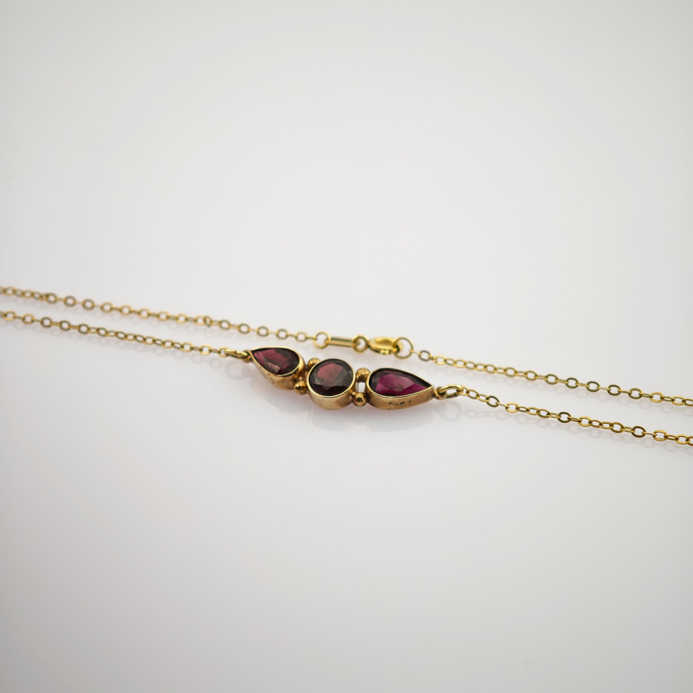 Elegantes Goldarmband mit drei dunkelroten Edelsteinen in Tropfen- und runder Form auf weißem Hintergrund