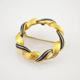 Fein gearbeitete runde Brosche mit gedrehtem Band aus strukturiertem Gold und dunkelblauen Emaille-Segmenten.