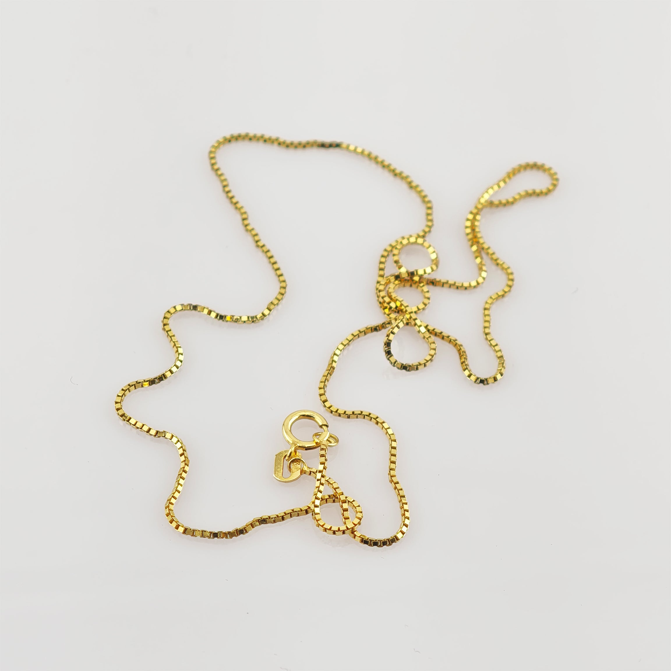 Feine, goldfarbene Boxkette mit rundem Federringverschluss vor weißem Hintergrund.