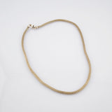 Feine Goldkette mit gewebter Mesh-Textur und Karabinerverschluss auf weißem Hintergrund.