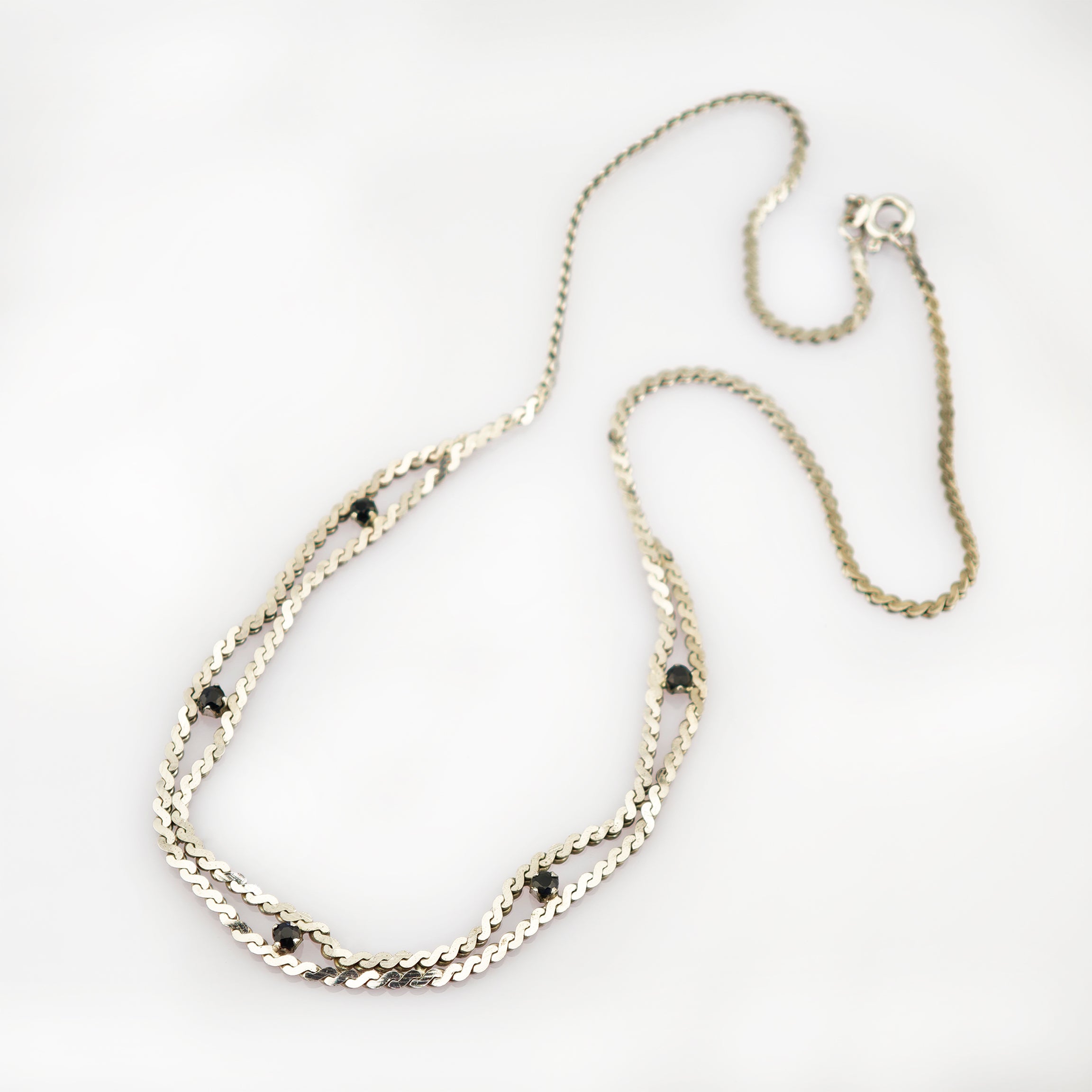 Feine Silberkette mit kleinen schwarzen Edelsteinen und sichtbarem Verschluss auf weißem Hintergrund.