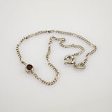 Feine Silberkette mit abwechselnd gedrehten und flachen Gliedern und kleinem rundem Anhänger mit tiefrotem Edelstein.