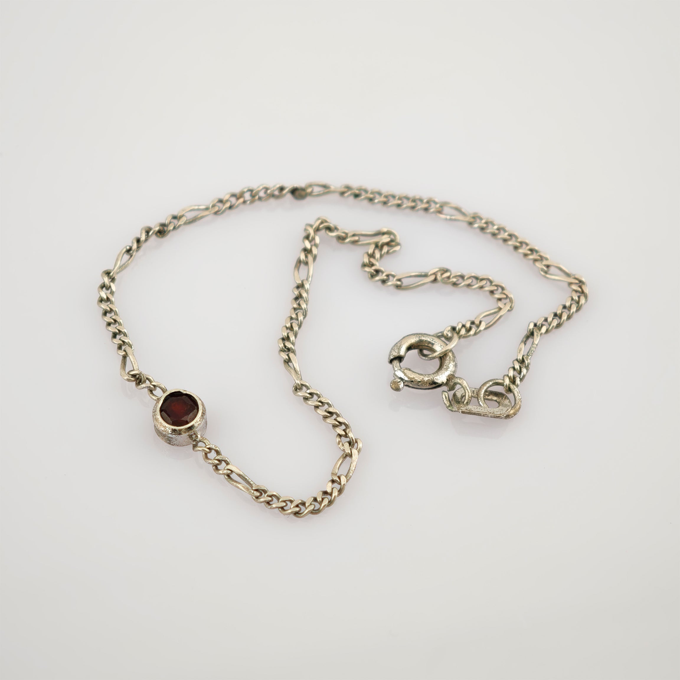 Feine Silberkette mit abwechselnd gedrehten und flachen Gliedern und kleinem rundem Anhänger mit tiefrotem Edelstein.